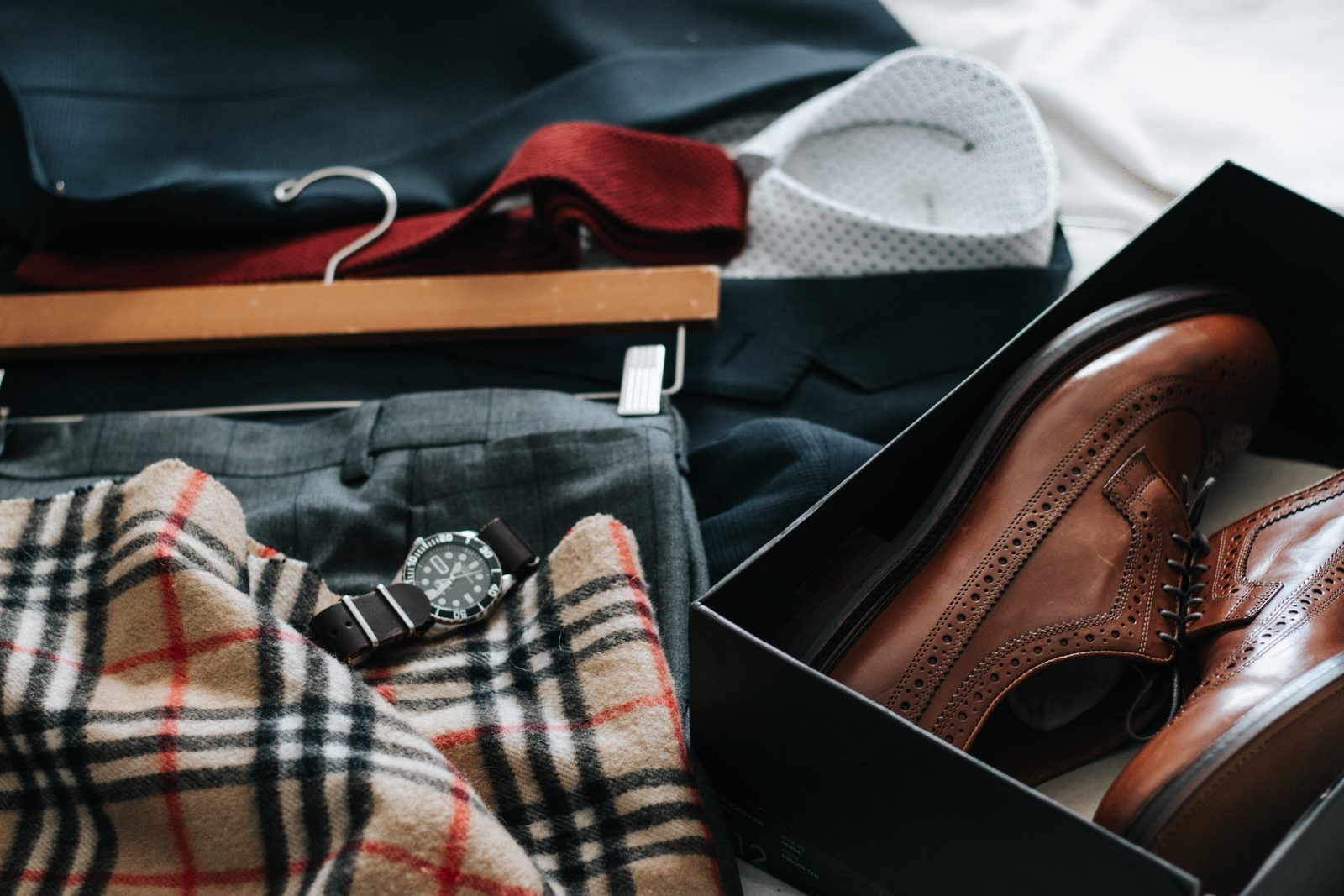 A wristwatch resting on folded tailoring beside a pair of brogues